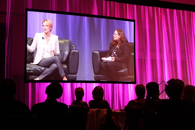 One of two large screens showing Amy Robach and Janelle Logan, Spectrum Health director of community engagement, on stage.
