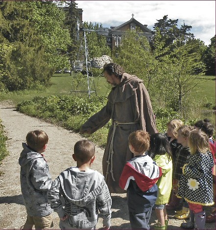 Sculptor Mic Carlson, dressed as St. Francis leads the children toward the Meditation and Sculpture Garden.