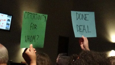 "Done Deal" and "Opportunity for Whom?" Audience members hold up signs at the first AmplifyGR town hall in 2017.