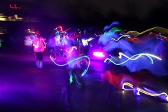 Athletes dressed in glow sticks and body paint run past.